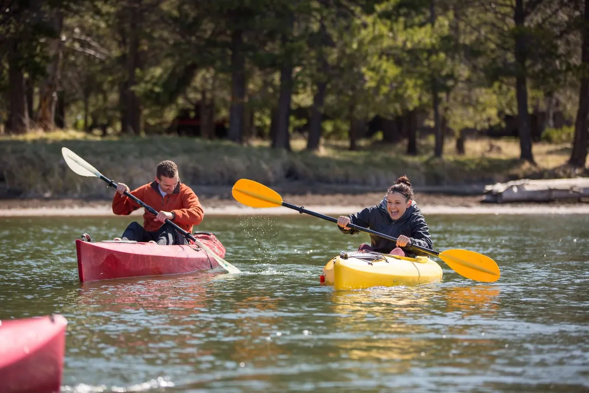 Two kayakers in colorful kayaks paddle through a serene natural landscape. The water and surrounding greenery suggest recreational opportunities and a spirit of adventure.