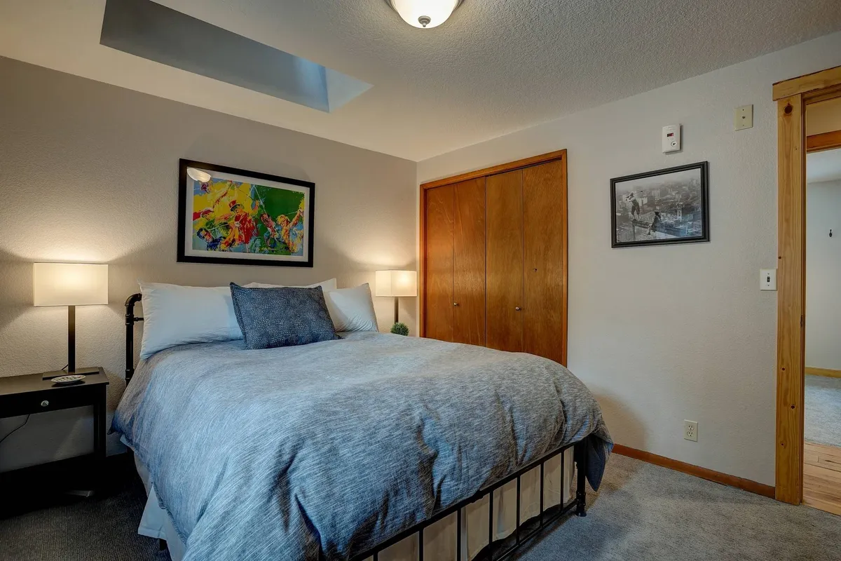 A bedroom with gray bedding, colorful artwork above the bed, and bedside lamps on both sides. The warm lighting and artistic touches create a cozy, serene environment ideal for relaxation and reading before sleep.