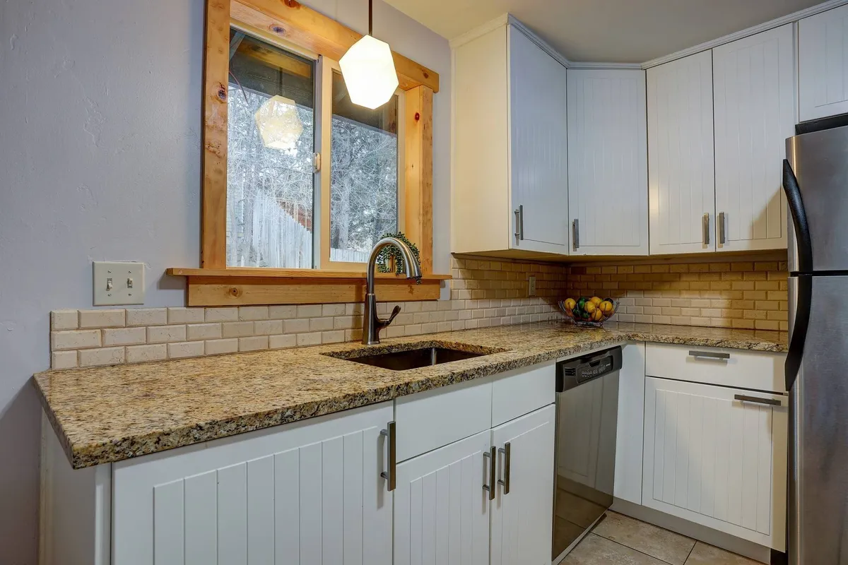 A modern, fully equipped kitchen with granite countertops, a sink, a window with a scenic view, a dishwasher, and a fruit bowl. The space is perfect for cooking together, enjoying coffee, or prepping meals for a group.