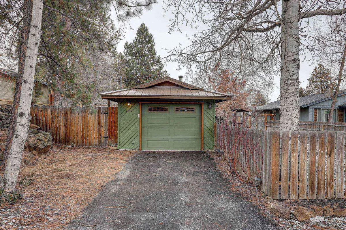 A rustic exterior shot of the home’s green garage door and wooden fence, set among aspen trees and a gravel driveway. The peaceful, nature-surrounded entrance hints at convenient access to gear storage and outdoor excursions.