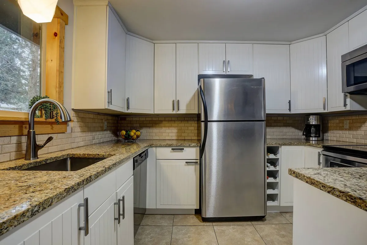 A welcoming kitchen featuring stainless steel appliances, granite countertops, and a window letting in natural light. The space is ready for meal prep or entertaining, capturing the essence of group cooking and shared feasts.