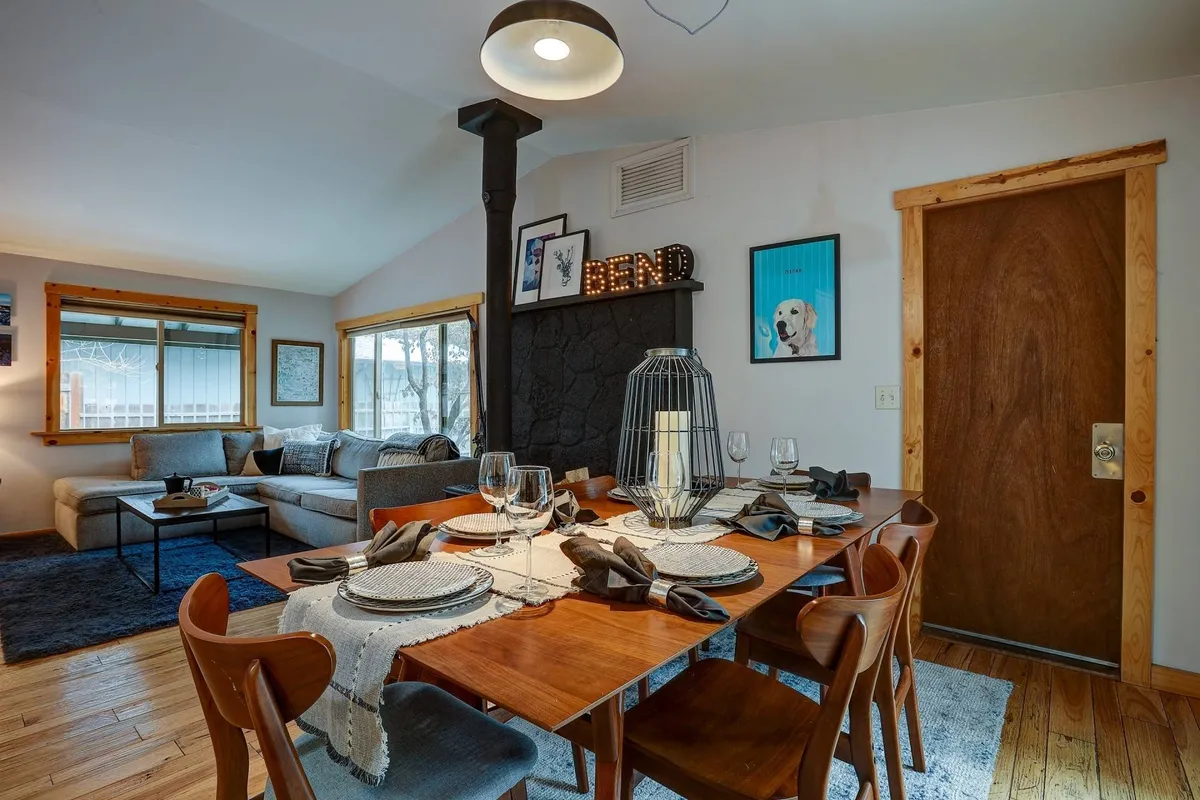 A stylish interior scene showing a dining table set with dinnerware, a stone fireplace, a comfortable sofa area, and decorative wall art. The ambiance is warm and inviting, ideal for family meals or relaxing after adventures.