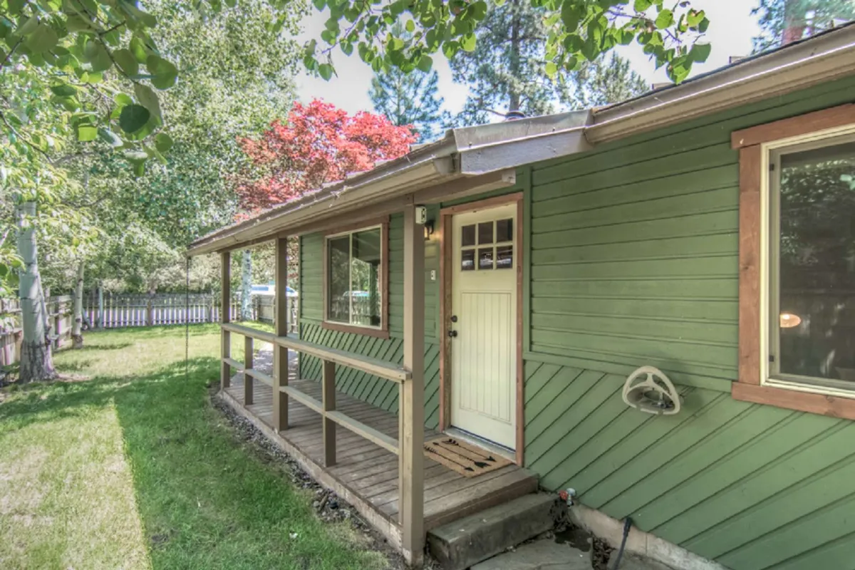 A welcoming front porch with green siding and a door entrance surrounded by lush trees. The cozy setting hints at outdoor relaxation, with opportunities to enjoy the natural beauty right outside the home.