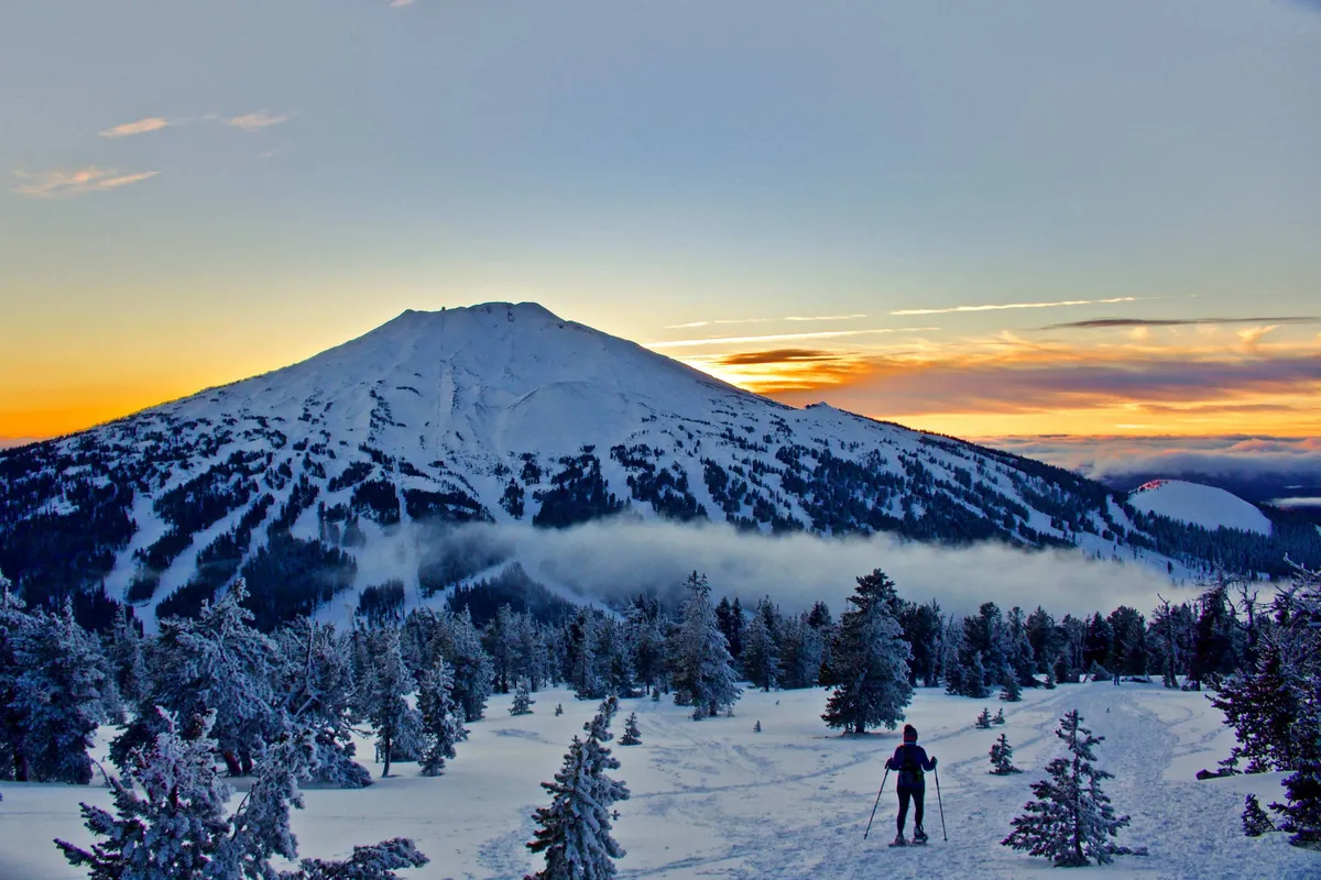 This exterior image captures a snow-covered mountain at sunset, with a skier active in the foreground. The vivid horizon and winter landscape evoke the outdoor adventure and natural beauty surrounding the home, underscoring the sense of place that Bend offers.