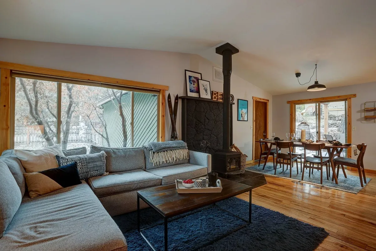 A spacious, open-concept living area featuring a comfortable sofa, a dining table, a cozy fireplace, and large windows letting in natural light. The area is designed for relaxing, dining, and socializing, with thoughtful decor adding to the inviting atmosphere.