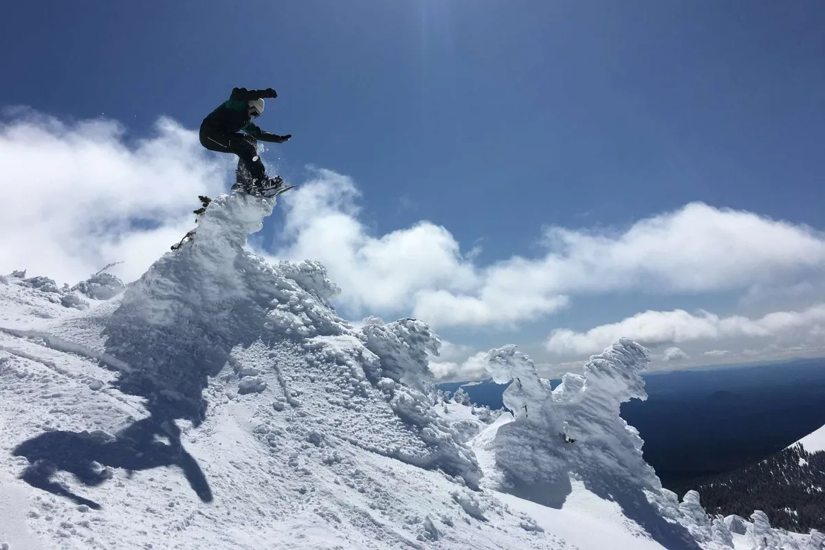 A snowboarder is captured mid-air against the backdrop of a snow-covered peak, with dramatic clouds swirling above. The landscape is blanketed in fresh snow, evoking a sense of winter adventure and excitement.