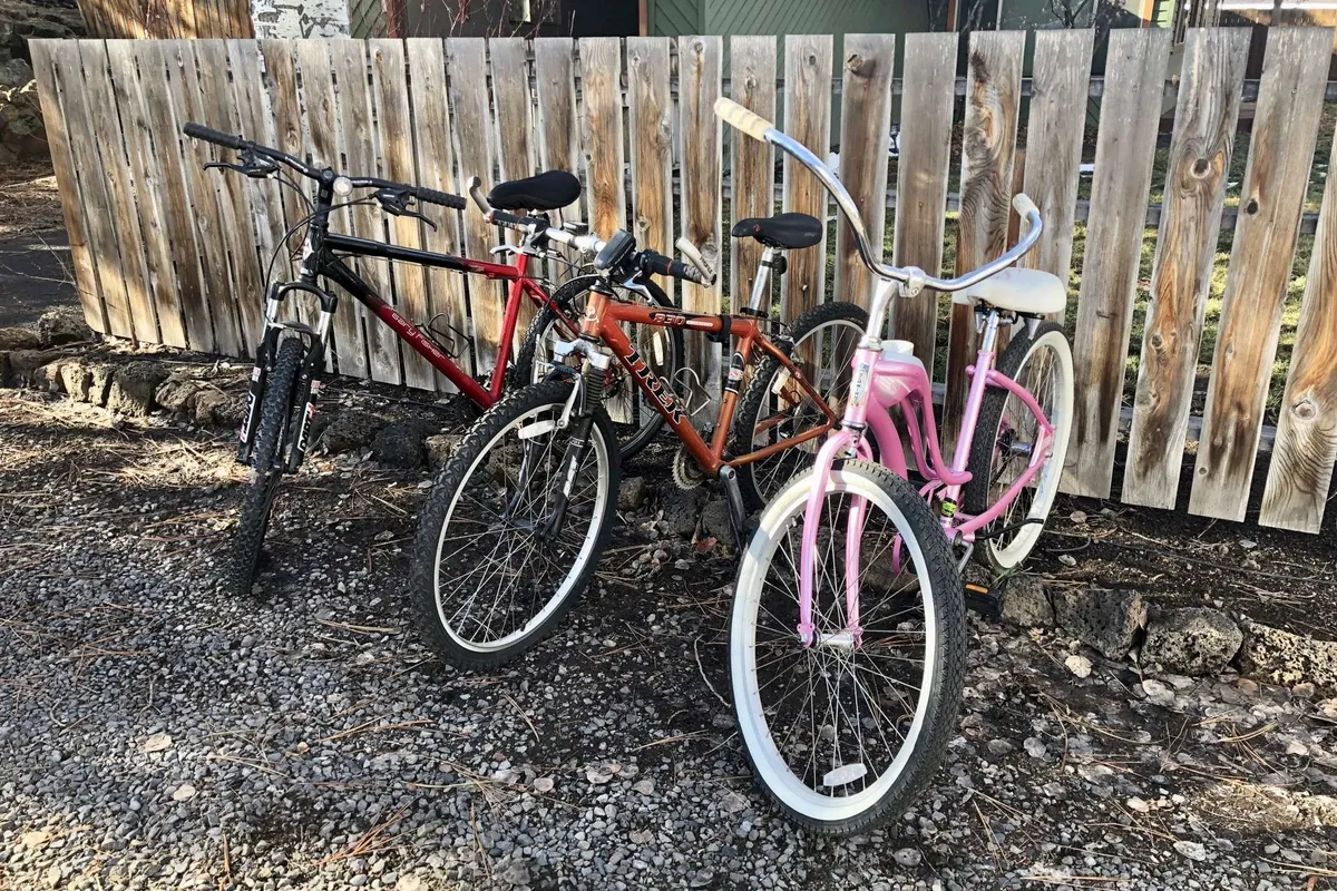 This image shows three bicycles lined up against a wooden fence on a gravel ground, evoking a sense of readiness for outdoor adventures. The casual arrangement and accessible placement suggest this area is ideal for quickly grabbing a bike and heading out, mirroring the section's emphasis on easy transitions between inside and outside activities.
